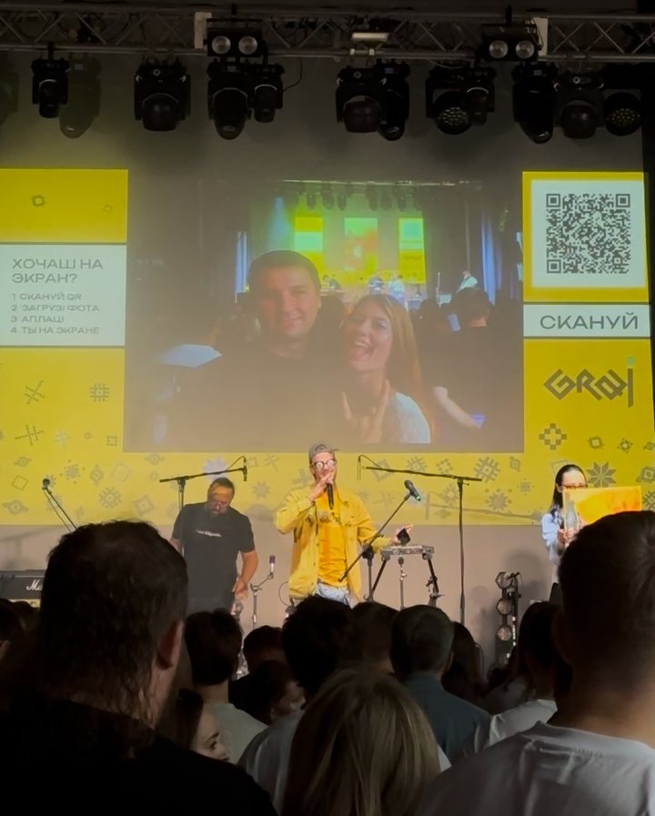 Graj: a projector with a photo of two guests, the QR panel and people on stage